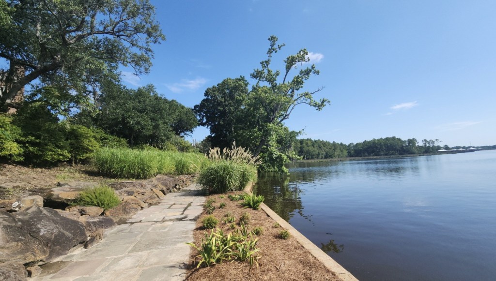 sidewalk through gardens beside river reflecting the sky
